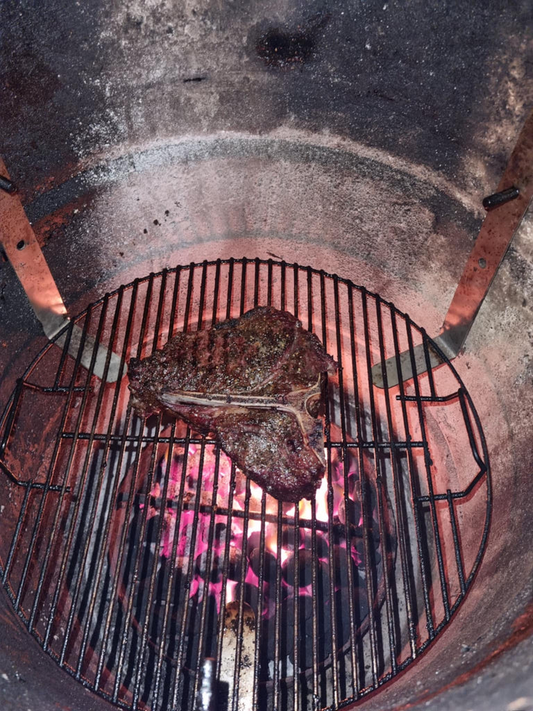 BBQ BOI Pit Barrel Grate Mates supporting a cooking grate with a grilled T-bone steak over hot charcoal in a Pit Barrel Cooker