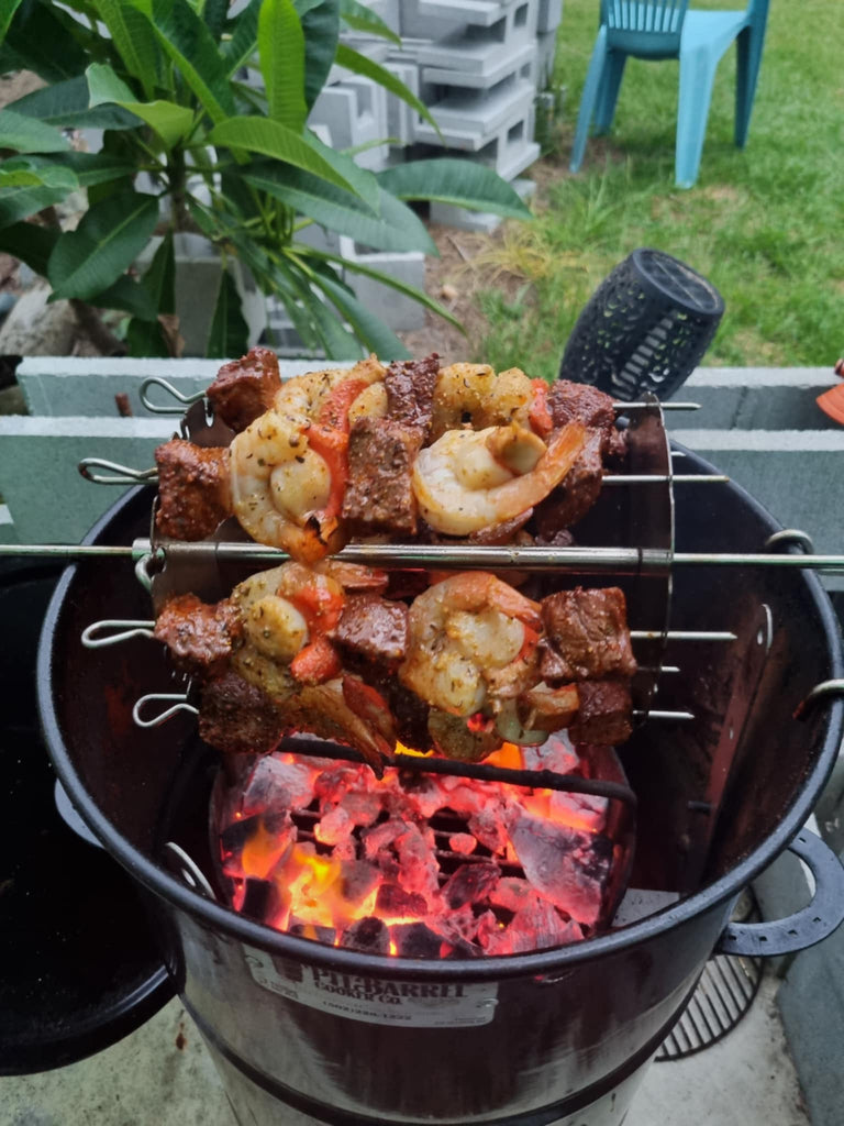 BBQ BOI Pit Barrel Grate Mates supporting barbecue skewers with beef, shrimp and vegetables over hot charcoal in a Pit Barrel Cooker